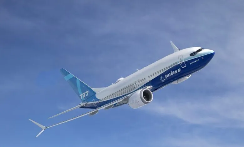 A white and blue Boeing 737 MAX airplane in flight against a clear blue sky.