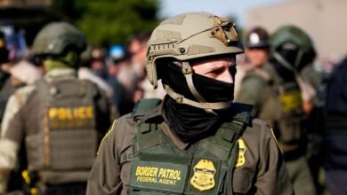 Close-up of a Border Patrol agent in tactical gear, wearing a helmet and face mask.