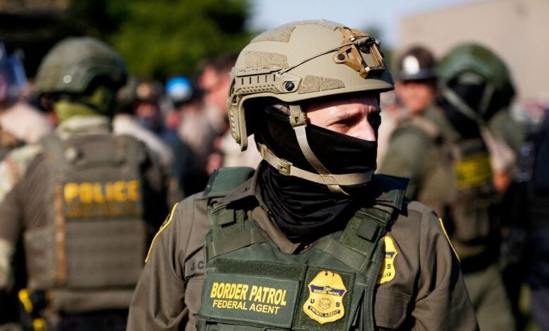 Close-up of a Border Patrol agent in tactical gear, wearing a helmet and face mask.