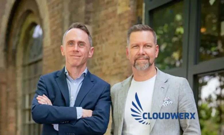 Two men in business attire posing outdoors with a brick building behind them.