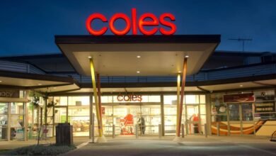 Coles supermarket entrance at dusk with illuminated signage and colorful pillars.