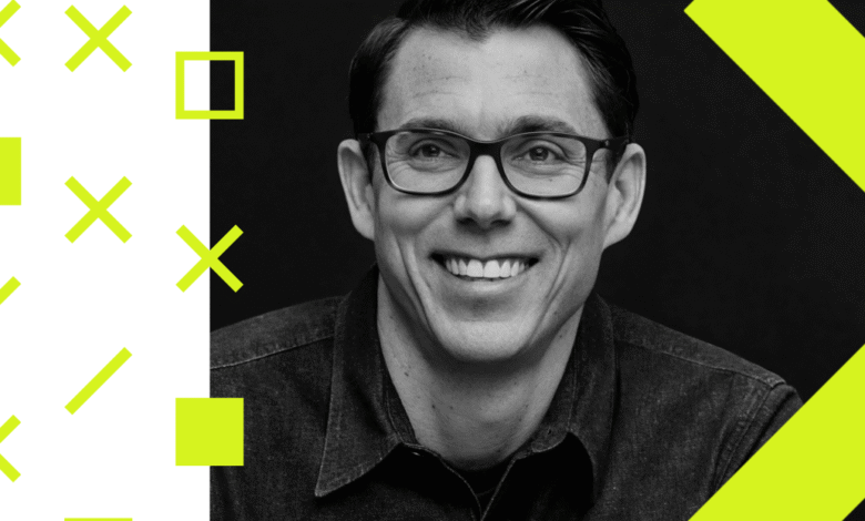Close-up portrait of a smiling man with glasses, wearing a denim shirt, against a dark background with graphic elements.