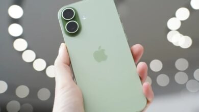 A hand holds a light green iPhone, showcasing its dual camera system and Apple logo.