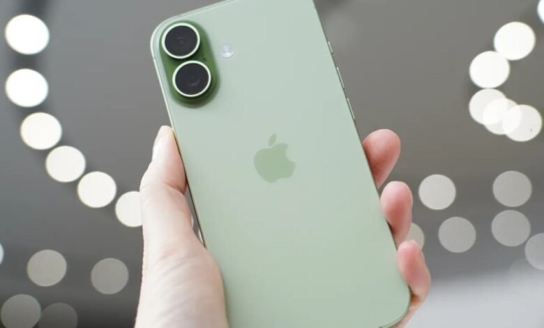 A hand holds a light green iPhone, showcasing its dual camera system and Apple logo.