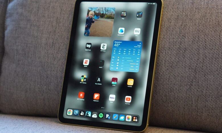 Close-up of a yellow iPad Pro displaying apps and widgets on a textured gray couch.
