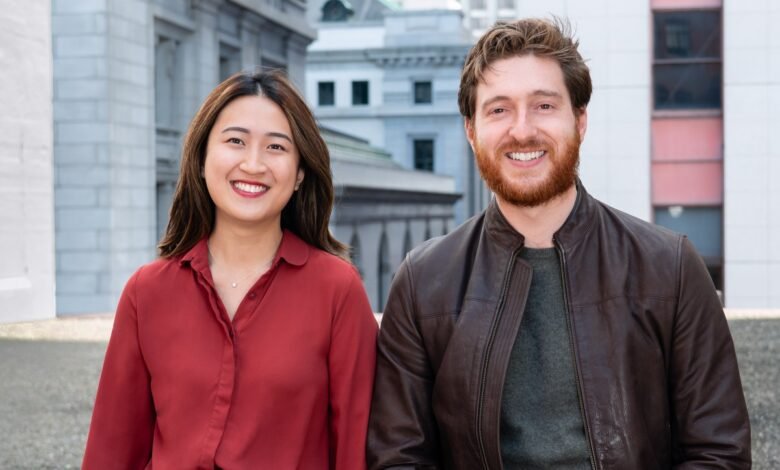 A smiling Asian woman in a red shirt and a smiling Caucasian man with a beard in a leather jacket.
