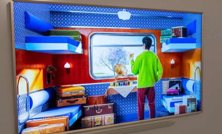 Person in a bright green sweater standing in a vintage train compartment, holding a drink.