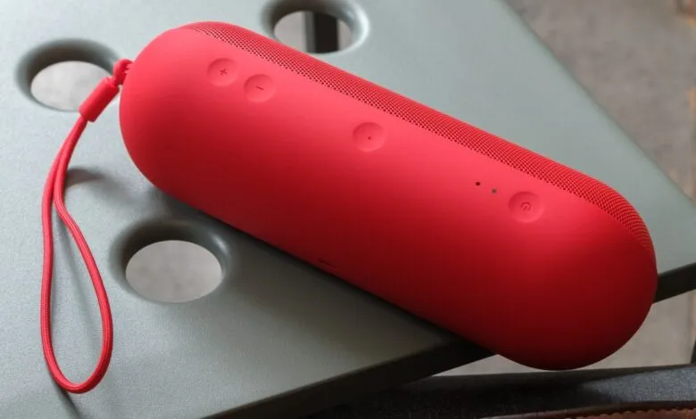 A bright red portable Bluetooth speaker with a red lanyard rests on a textured gray surface.