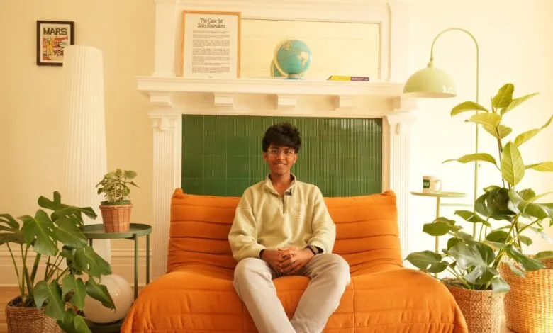 Young man sitting on an orange couch in a brightly lit room with plants.