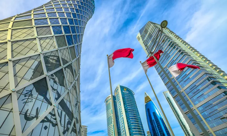 Modern skyscrapers and Qatari flags against a bright blue sky.