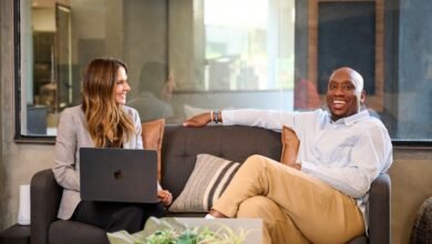 A woman with a laptop and a man sitting on a couch in a modern office setting.