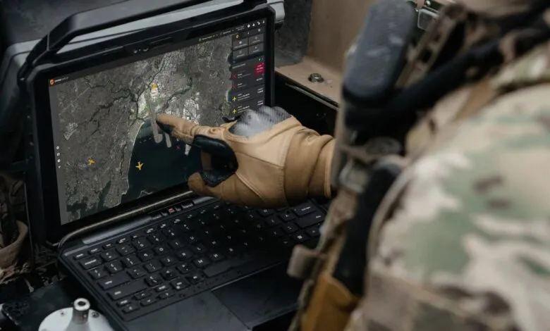 Soldier in camouflage points at a drone surveillance map on a rugged tablet.