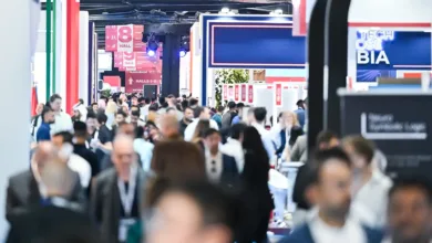 Crowd of people walking through a busy exhibition hall with signs for different halls.