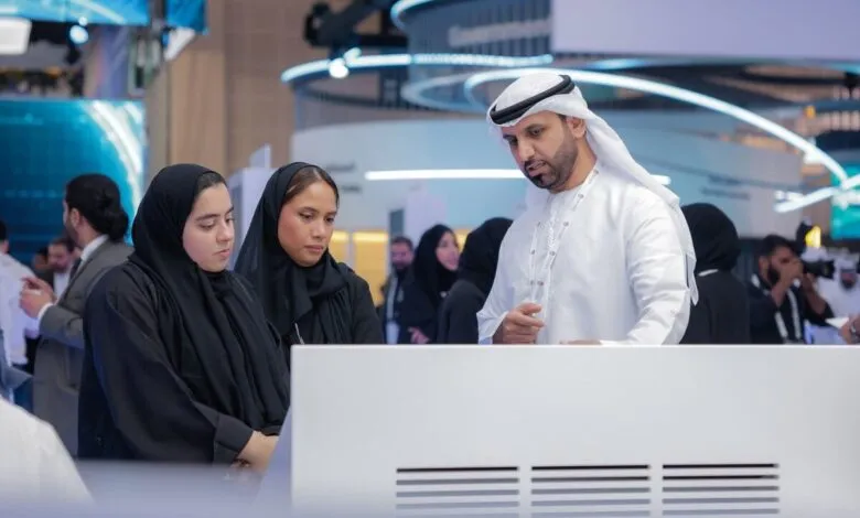 Man in traditional Emirati attire explains something on a screen to two women in hijabs.
