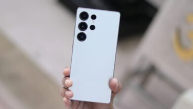 A hand holds a light blue Samsung Galaxy S25 Ultra smartphone, showcasing its rear camera array.