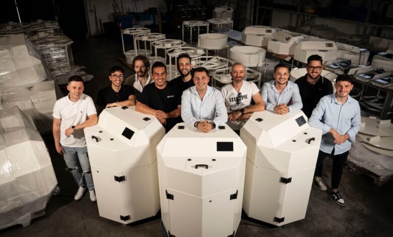 A team of ten men posing with large white polygonal machines in a workshop.