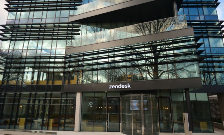Modern glass-fronted Zendesk office building with reflections of trees and sky.