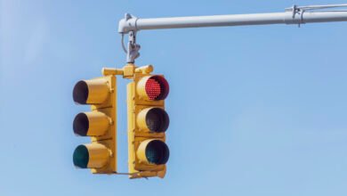 Yellow traffic lights with the red light illuminated against a clear blue sky.