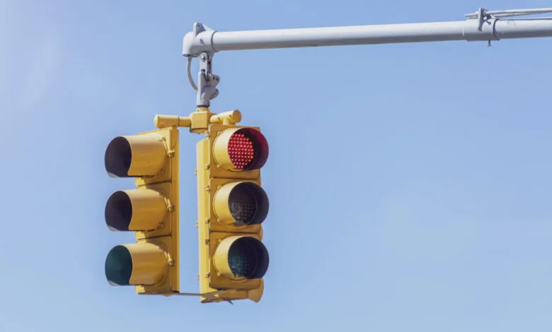 Yellow traffic lights with the red light illuminated against a clear blue sky.