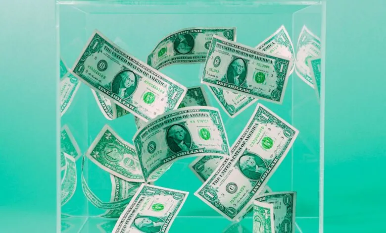One dollar bills floating inside a clear acrylic box against a teal background.