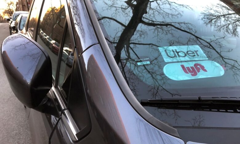 Uber and Lyft stickers on a car windshield with tree branches reflected.
