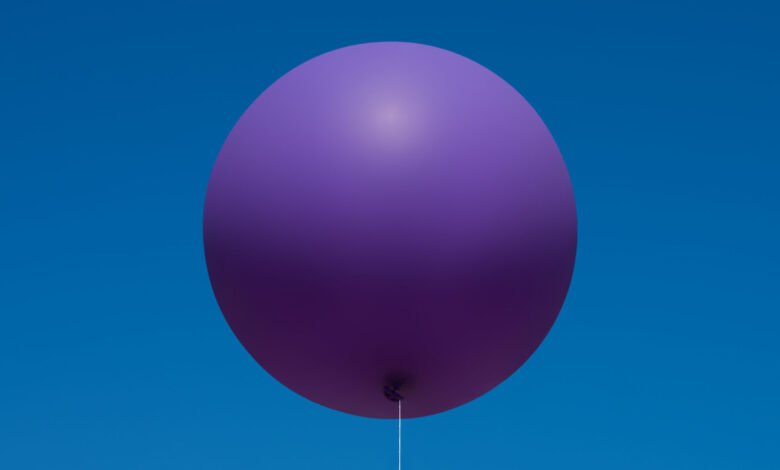 A single, large purple balloon floats against a clear blue sky.