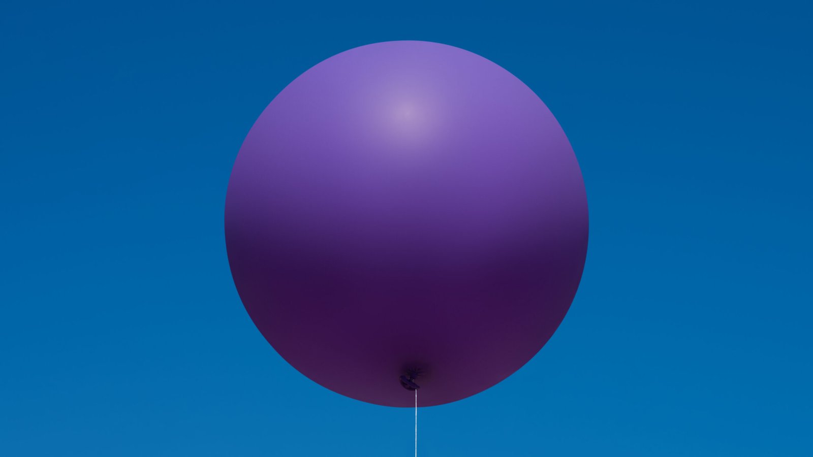A single, large purple balloon floats against a clear blue sky.