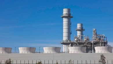 Modern industrial power plant with cooling towers and smokestacks against a clear blue sky.