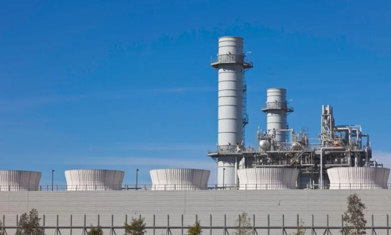 Modern industrial power plant with cooling towers and smokestacks against a clear blue sky.