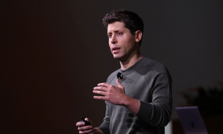 Man in a grey sweater speaking on stage with a microphone and holding a clicker.