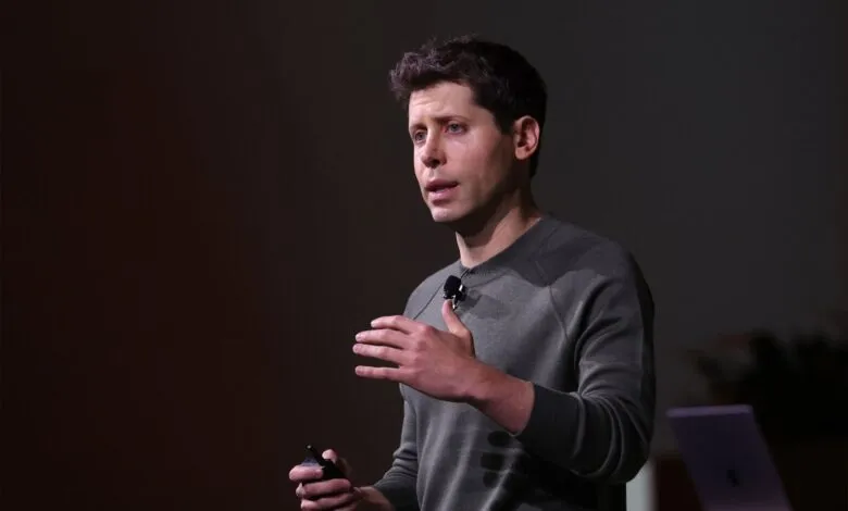Man in a grey sweater speaking on stage with a microphone and holding a clicker.