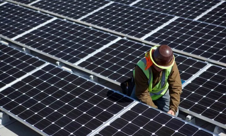 Worker installing solar panels on a rooftop under a bright sky.