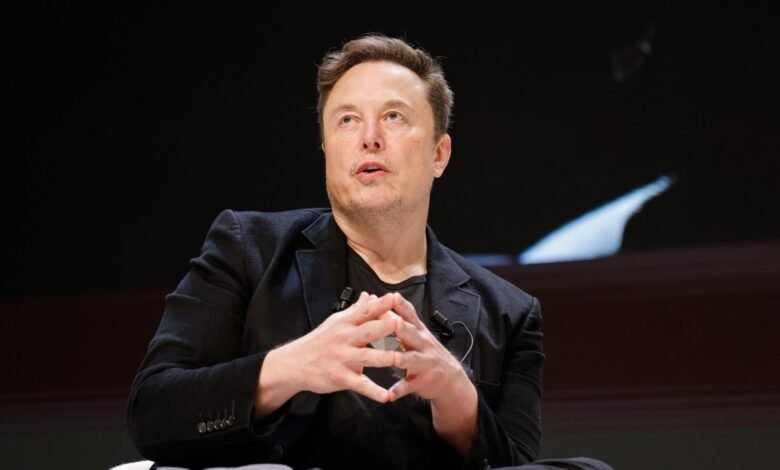 Elon Musk speaking with hands clasped in front of him.