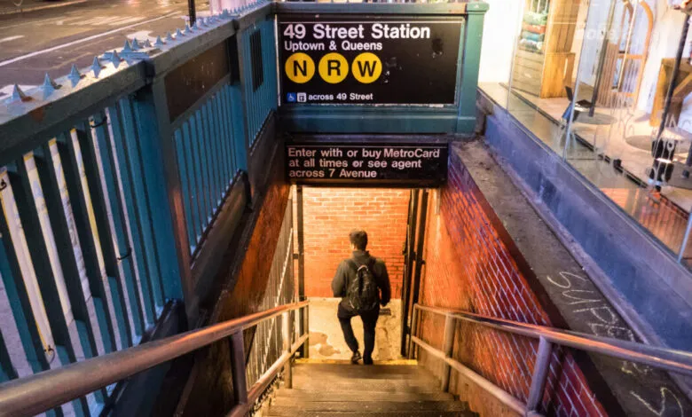 Man descending stairs into a brightly lit subway station entrance at night.