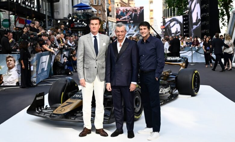 Three men in suits stand next to a Formula 1 race car on a red carpet.