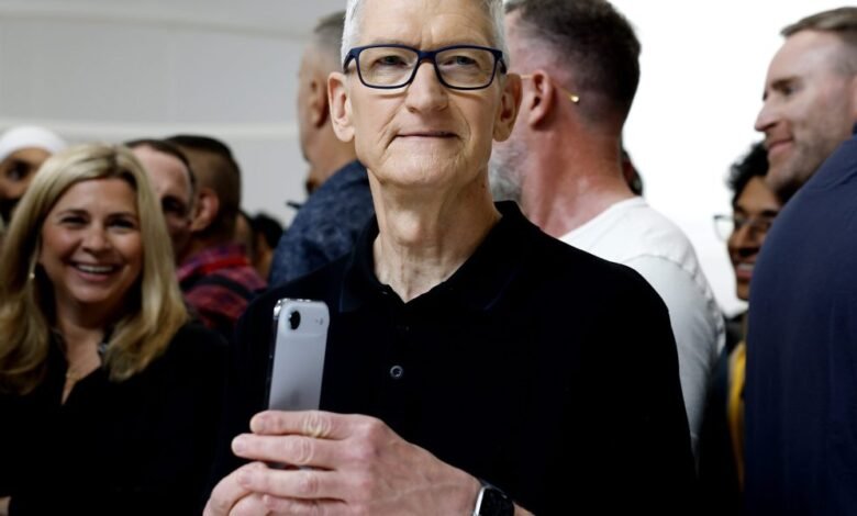 Tim Cook holding an iPhone, smiling at the camera surrounded by people.