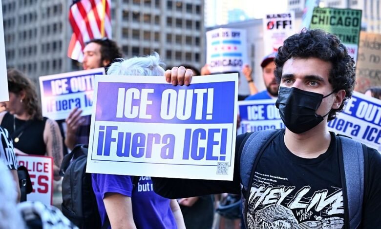 Man in black mask holds sign reading 'ICE OUT! ¡Fuera ICE!' at a protest.