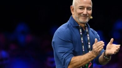 Jeff Bezos speaking on stage with a microphone, wearing a blue shirt and a lanyard.