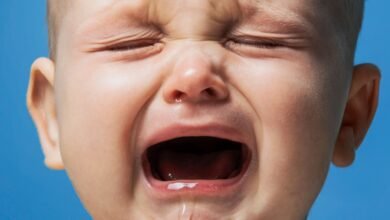 Close-up of a baby's face crying with eyes squeezed shut and mouth wide open.