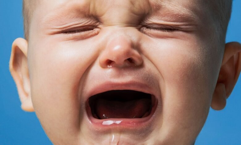 Close-up of a baby's face crying with eyes squeezed shut and mouth wide open.