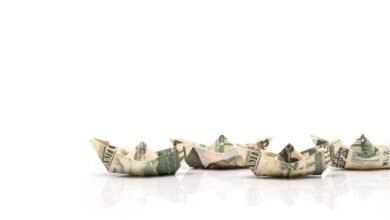 Origami boats made from US dollar bills lined up on a white surface.