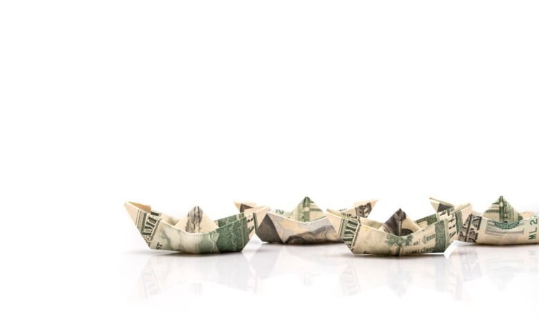 Origami boats made from US dollar bills lined up on a white surface.