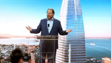 Marc Benioff speaks at a podium with Salesforce Tower displayed on a large screen behind him.