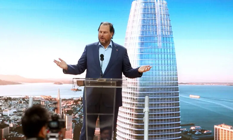 Marc Benioff speaks at a podium with Salesforce Tower displayed on a large screen behind him.
