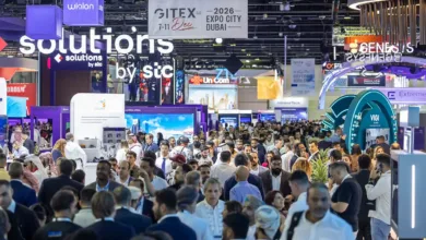 Crowded exhibition hall with many attendees and booths, featuring large signs for GITEX and various tech companies.