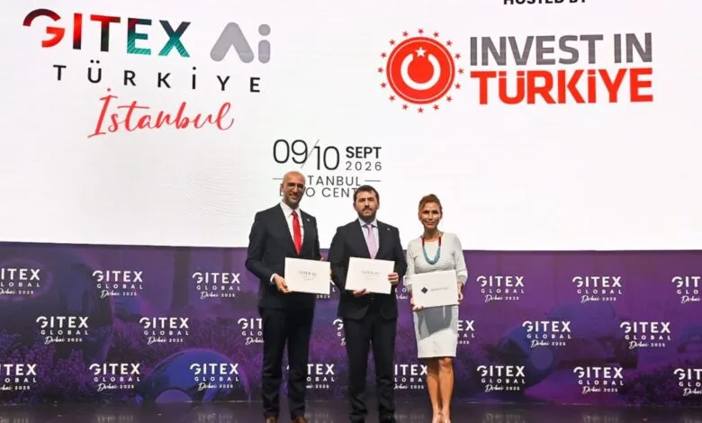 Three people in formal attire holding certificates on a stage with event branding.