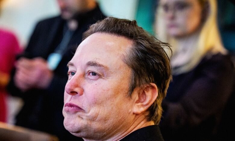 Close-up profile of Elon Musk looking intently to the left, with blurred figures in the background.