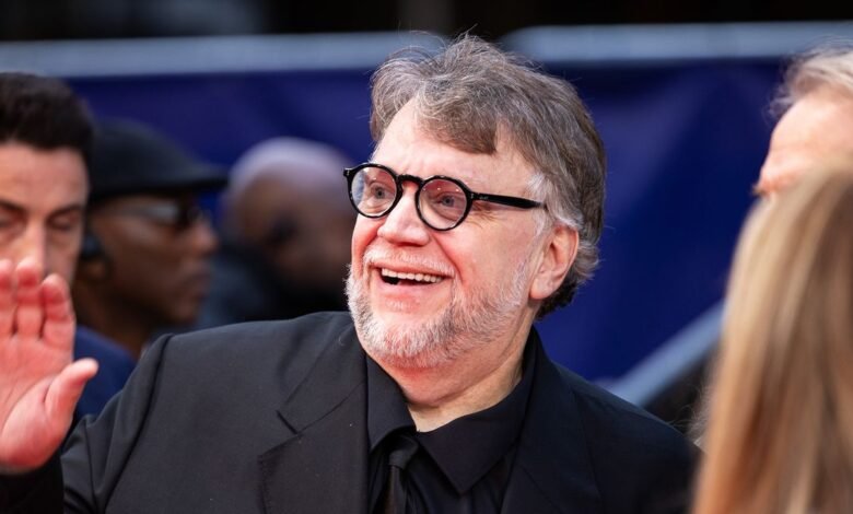 Guillermo del Toro waves to fans, smiling broadly with round glasses.