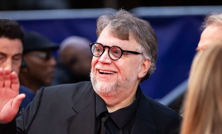 Guillermo del Toro waves to fans, smiling broadly with round glasses.