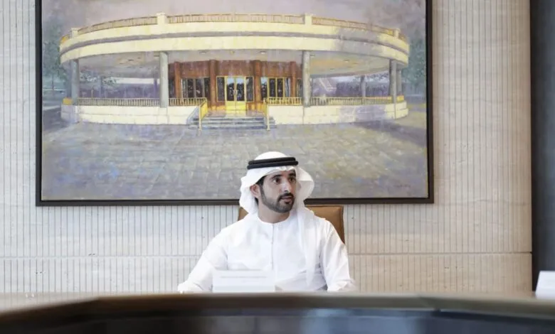 Sheikh Hamdan bin Mohammed Al Maktoum in traditional white attire sits in a modern office.